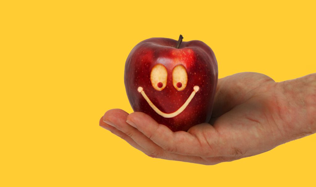 ein Apfel auf einer Hand mit einem lachenden Gesicht