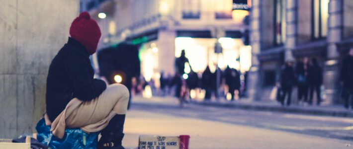 Ein Mann auf einer Plasiktüte bittet um Geld in einer Einkaufstrasse