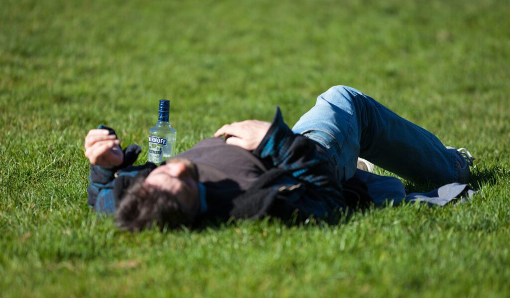 Eine betrunkene Person auf einer Wiese mit einer Wodkaflasche