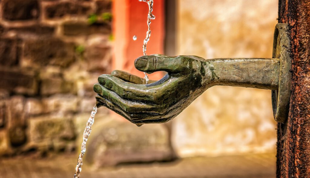 Eine Hand an einem Brunnen mit Wasser