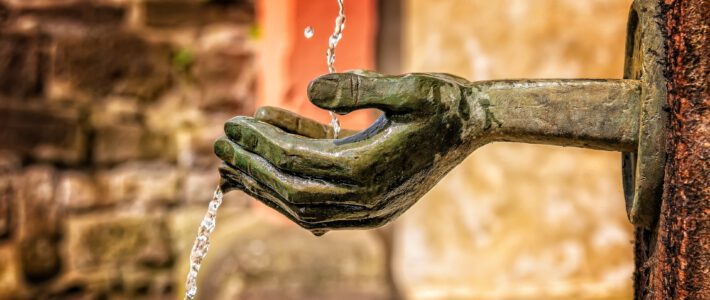 Eine Hand an einem Brunnen mit Wasser