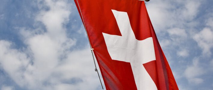 Eine Flagge der Schweiz vor blauem Himmel mit weissen Wolken