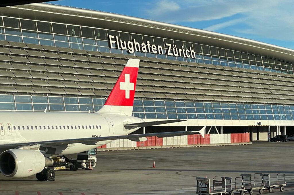 Logo des Flughafens Zürich am Hauptgebäude und ein Flugzeug der Swiss im Vordergrund