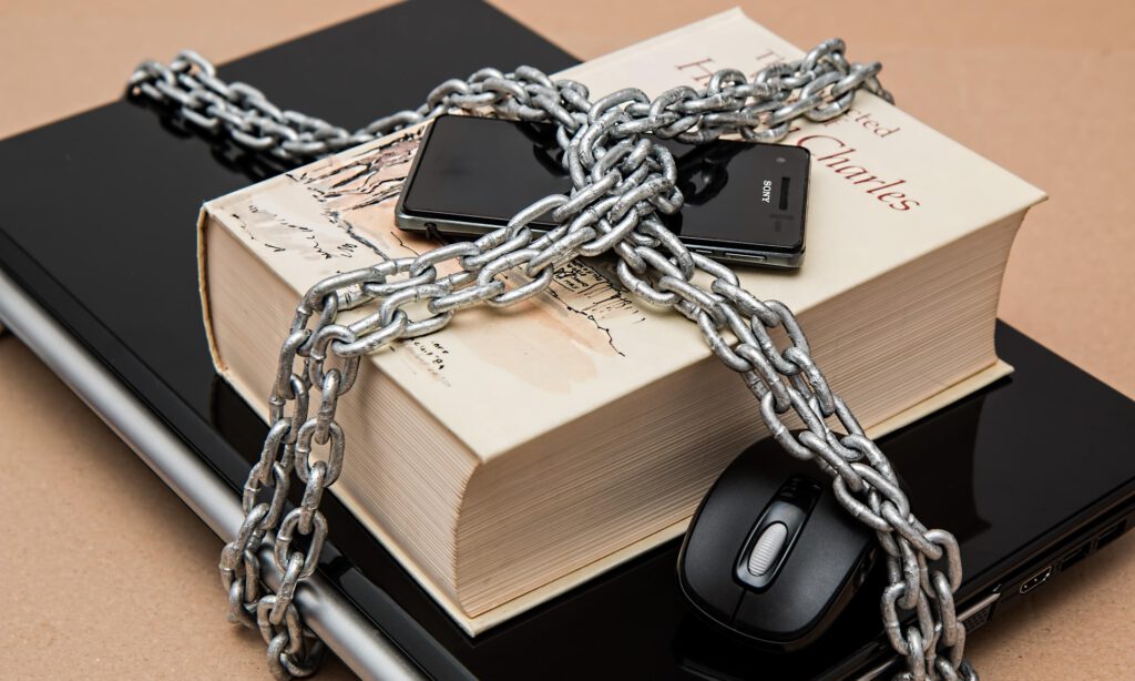 Ein Notebook, Buch und Handy mit einer Kette umschlungen
