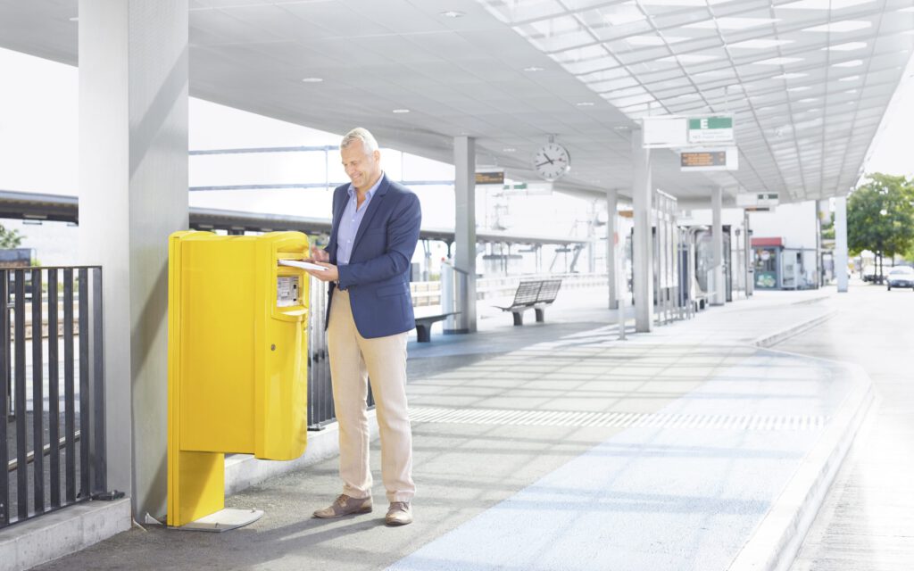Briefkasten der Post an einem Bahnhof mit einem Mann