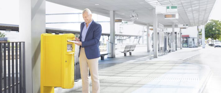 Briefkasten der Post an einem Bahnhof mit einem Mann
