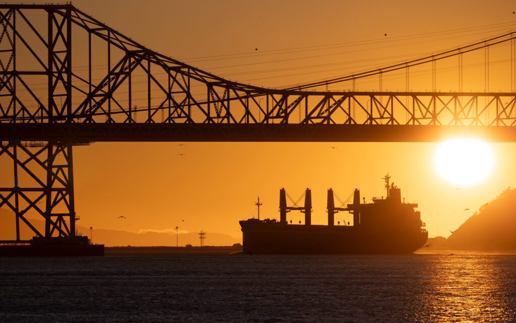 Ein Schiff vor einer Brücke im Sonnenuntergang