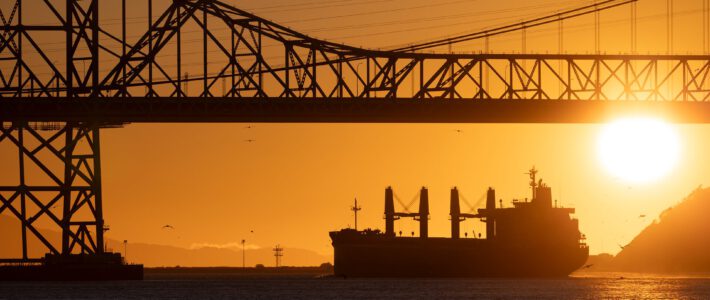 Ein Schiff vor einer Brücke im Sonnenuntergang