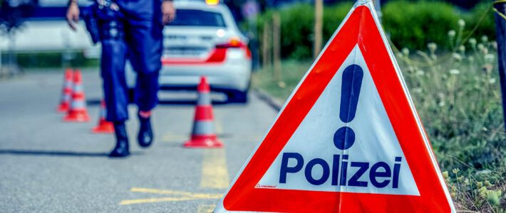 Weko deckt neues Baukartell auf Ein Polizei-Schild sowie ein Polizeifahrzeug auf einer Strasse