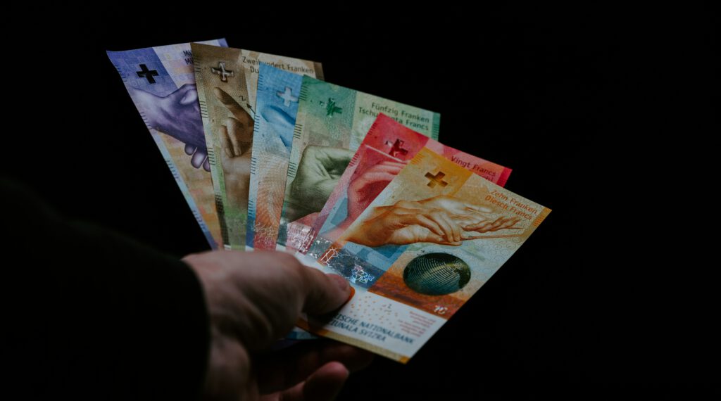 Banknoten von Schweizerfranken in einer Hand vor schwarzem Hintergrund