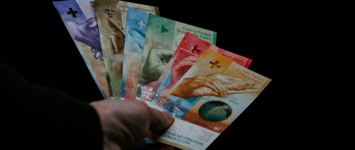 Banknoten von Schweizerfranken in einer Hand vor schwarzem Hintergrund