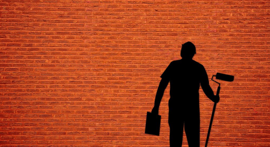Ein Maler mit Farbe und Pinsel vor einer orangen Wand