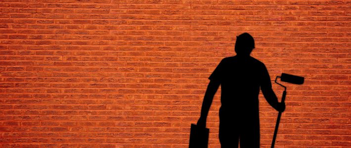 Ein Maler mit Farbe und Pinsel vor einer orangen Wand