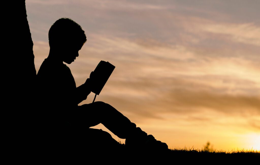 Ein Kind mit einem Buch an einem Baum in der Abendsonne
