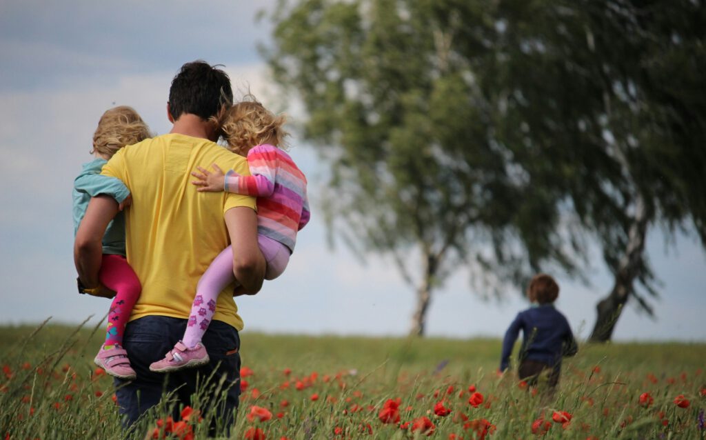 Ein Mann mit zwei Kindern auf den Armen in einem Blumenfeld