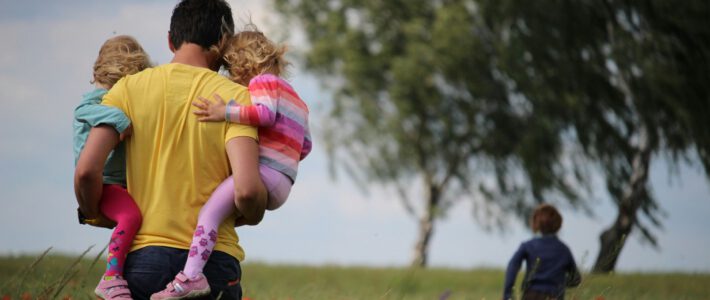 Tausende Schweizer pfeifen auf das Geld für Eltern Ein Mann mit zwei Kindern auf den Armen in einem Blumenfeld