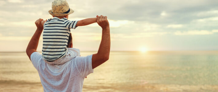 Schweizer sehnen sich 2026 stärker ins Ausland Ein Mann mit einem Kind auf den Schultern am Meer beim Sonnenuntergang