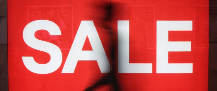 Grundlage für weitere Rabattschlachten gelegt Ein Sale-Schild in einem Schaufenster mit einer Person davor