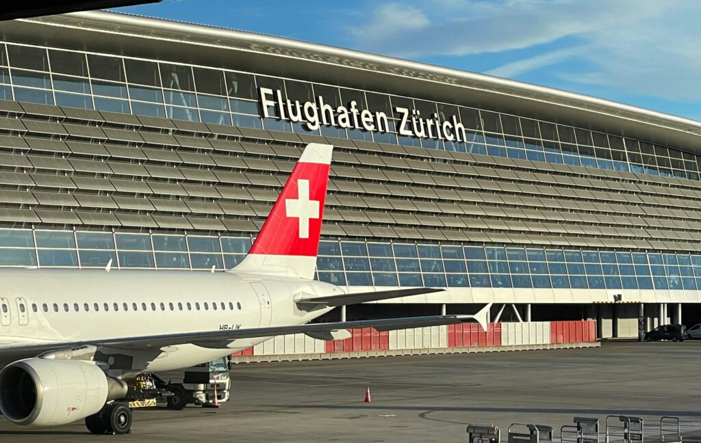 Logo Flughafen Zürich am Hauptgebäude und ein Flugzeug der Fluggesellschaft Swiss mit Schweizerkreuz