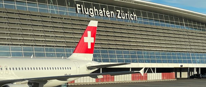 Logo Flughafen Zürich am Hauptgebäude und ein Flugzeug der Fluggesellschaft Swiss mit Schweizerkreuz