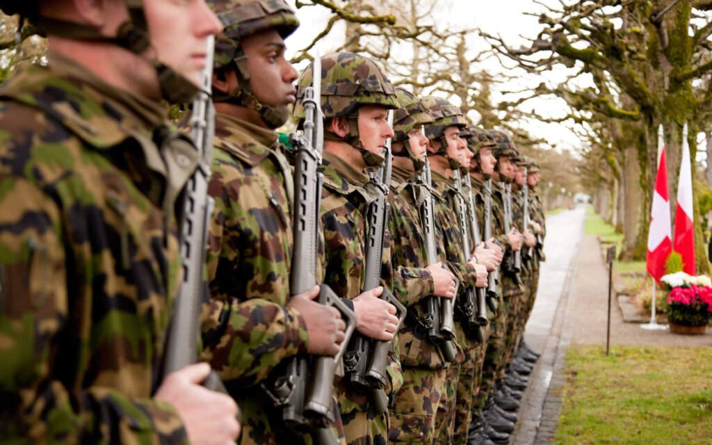 Schweizer Soldaten mit Sturmgewehren vor Schweizer Flaggen