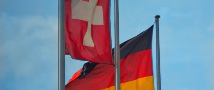 Schweizer ticken beim Geld anders als Deutsche Eine Schweizer und eine deutsche Flagge im Wind