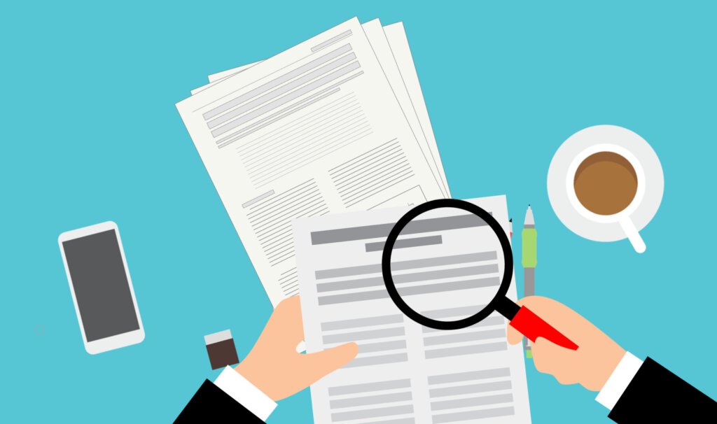 Eine Lupe über Dokumenten mit Kaffeetasse und Handy