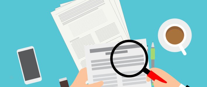 Eine Lupe über Dokumenten mit Kaffeetasse und Handy