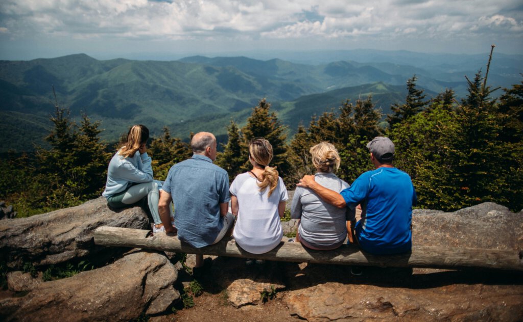 Drei Generationen sitzen auf einer Bank vor Bergen