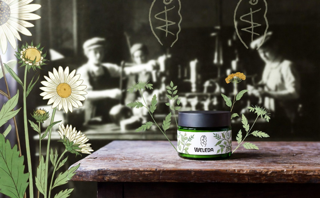 Blumen und ein Weleda-Produkt auf einem Tisch vor verschwommenen Arbeitern im Hintergrund