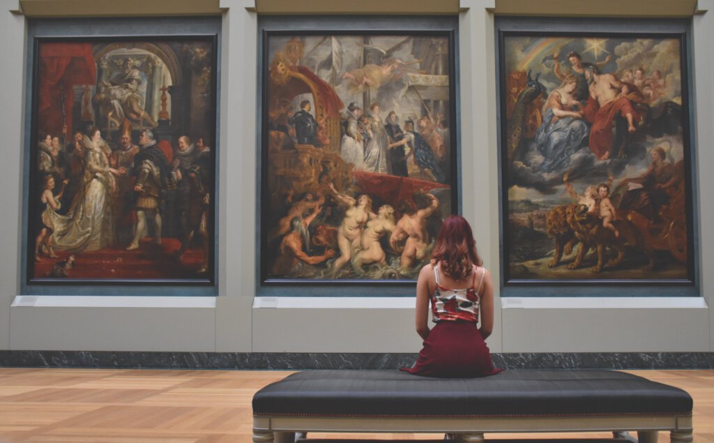 Eine Frau sitzt vor drei Gemälden