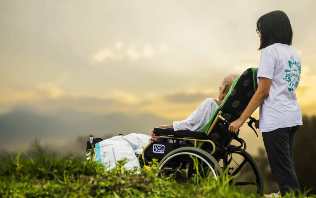 Eine Frau im Rollstuhl mit einer Pflegekraft vor Alpenpanorama