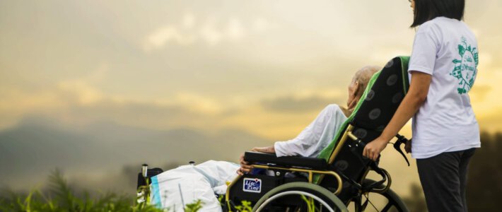 Eine Frau im Rollstuhl mit einer Pflegekraft vor Alpenpanorama