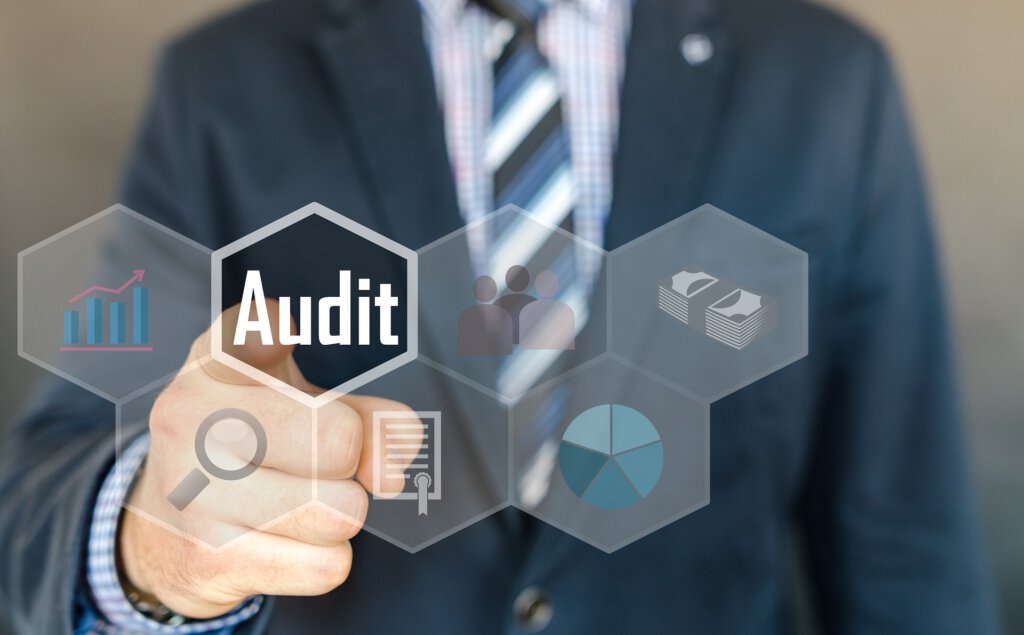 Ein Mann im Anzug mit einem Finger nach vorne auf das Wort Audit