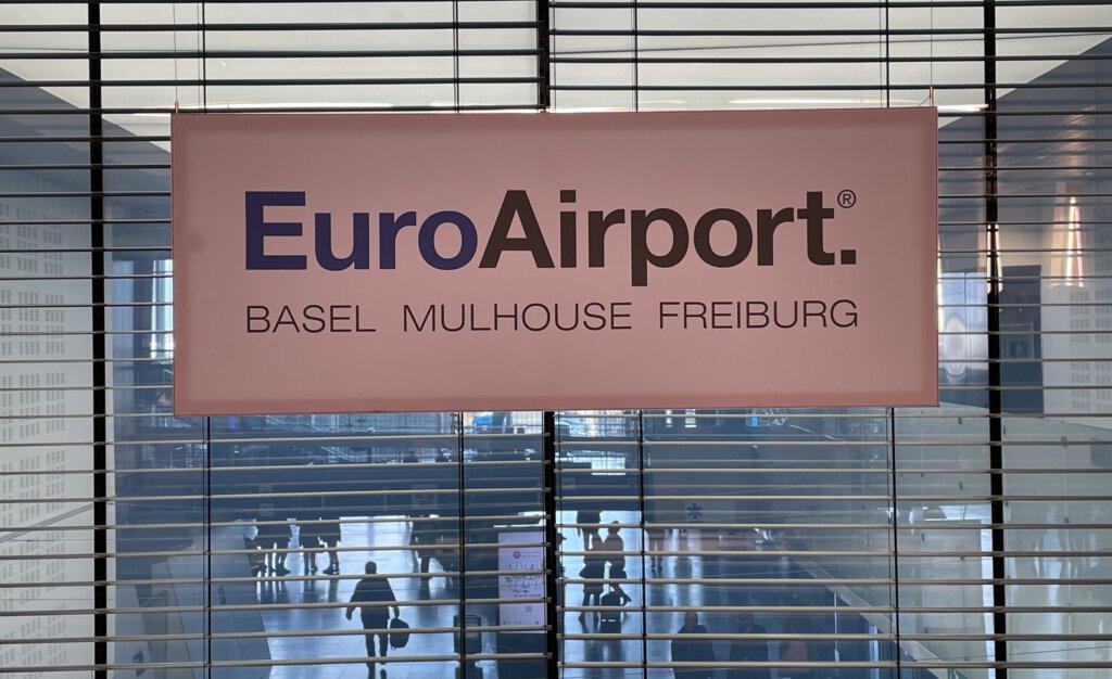 Logo vom Euroairport an einer Medienkonferenz mit Passagieren im Hintergrund