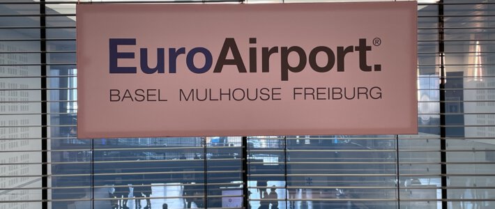 Euroairport weit abgeschlagen im Sicherheits-Ranking Logo vom Euroairport an einer Medienkonferenz mit Passagieren im Hintergrund