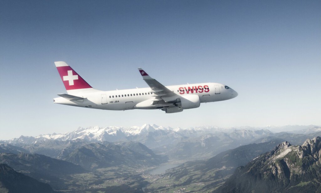 Ein Airbus A220 der Swiss in der Luft mit Alpen im Hintergrund