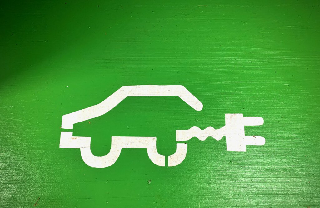 Ein symbolisches Auto mit Stromanschluss vor grünem Hintergrund