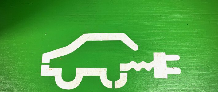 Viele Plug-in-Hybride sind schwerere Verbrenner Ein symbolisches Auto mit Stromanschluss vor grünem Hintergrund