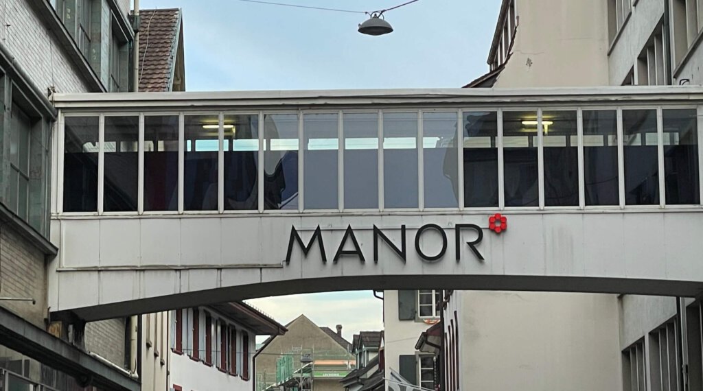 Logo von Manor an einem Gebäudeübergang in Basel