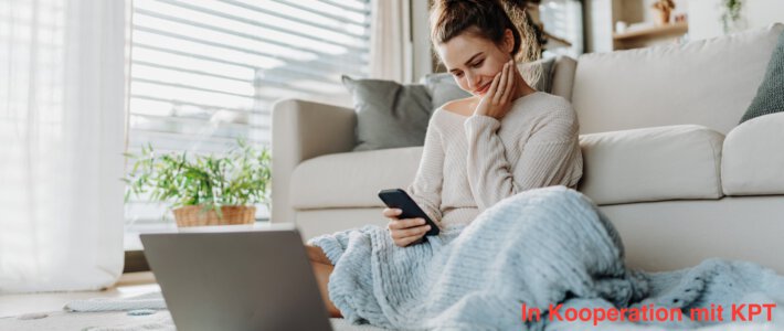 Eine Frau schaut vor ihrem Notebook auf ihr Smartphone