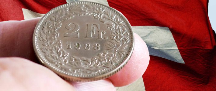 Schweizer halten ihr Geld vermehrt zusammen Schweizer Frankenmünze auf zwei Fingern vor einer Schweizerflagge